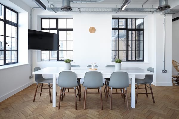 Office space with long table, chairs, television and windows. 